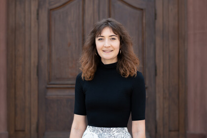 Portrait of Jessica Müller. She is standing in front of a door, waering a black shirt.