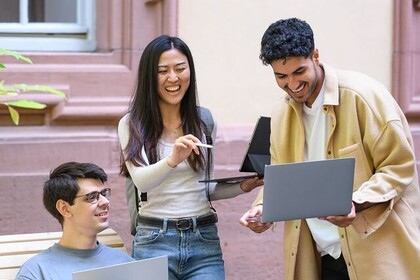 Eine Studentin und zwei Studenten stehen in einem der Schlosshöfe. Alle Drei haben einen aufgeklappten Laptop in der Hand und lachen freudig. Link: Instagram-Post Intensivkurs zur Studienorientierung