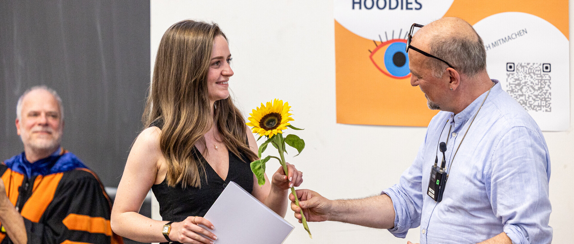 Studentin erhält Urkunde und Blume.