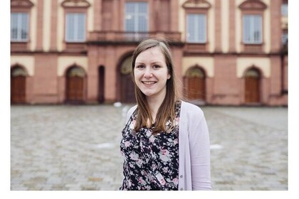 Porträt von Natalie Roik, die ihren Master Kultur- und Wirtschaft an der Uni Mannheim gemacht hat und darüber in der Reihe #testimonialtuesday erzählt. Roik hat lange braune Haare und trägt ein geblümtes Top mit einer rosafarbenen Strickjacke. Sie lacht fröhlich in die Kamera. Link: Instagram testimonialtuesday