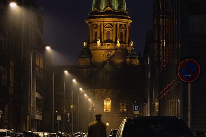 Blick auf den Wasserturm in Mannheim bei Nacht. Links und rechts stehen parkende Autos und eine Person läuft auf der Straße.