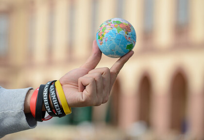 Eine Hand hält einen kleinen Weltkugelball mit zwei Fingern in die Luft.