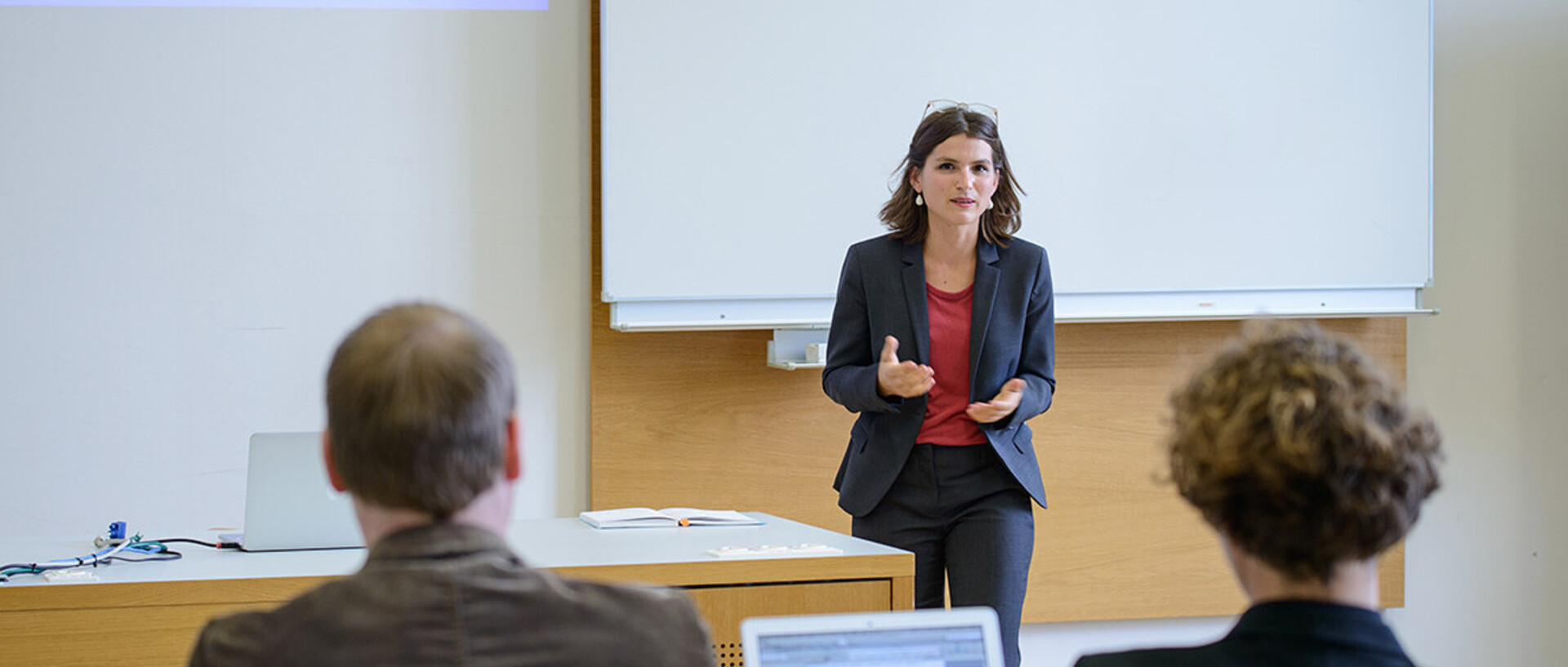 Eine Frau spricht am Pult vor zwei Zuhörern in der Universität.