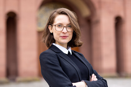Portrait von Svenja Behrend. Sie trägt einen schwarzen Blazer und steht vor einem teil des Schlosses.