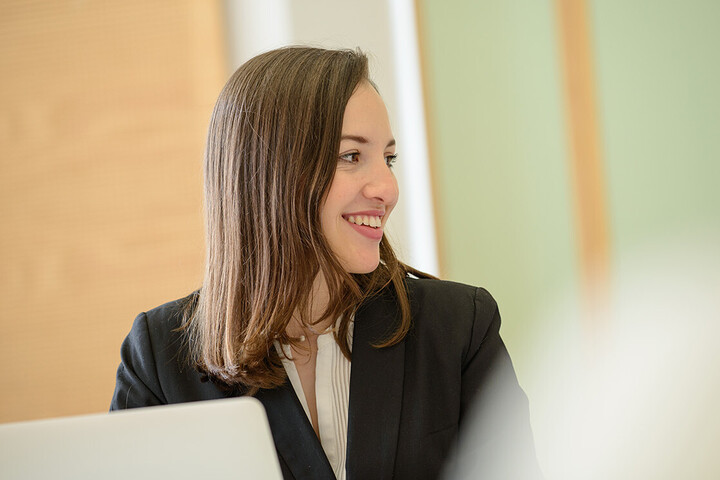 Side portrait of a smiling woman with brown hair, dressed in a white blouse and black blazer. 