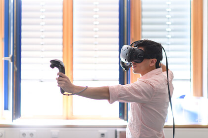 Ein Mann trägt eine Virtual Reality Brille, hält in jeder Hand einen Controller und spielt damit ein Spiel.
