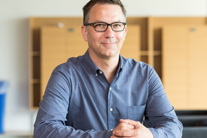 Portrait von Matthias Doepke. Er trägt ein blau-graues, langärmeliges Hemd. 