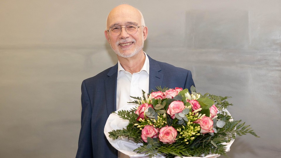 Thomas Puhl trägt einen Anzug und hält einen Blumenstrauß in den Händen.