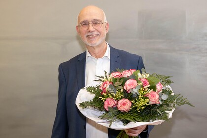 Thomas Puhl trägt einen Anzug und hält einen Blumenstrauß in den Händen.