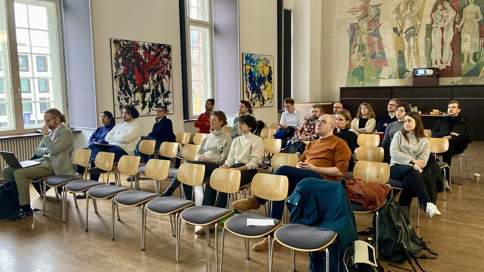 Die ca. 25 Teilnehmenden des Speed Datings sitzen in Stuhlreihen im Fuchs Festsaal