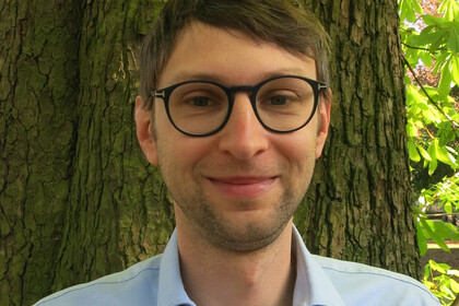 Portrait von Roni Lehrer. Er trägt eine Brille und ein hellblaues Hemd.