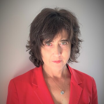 Irena Kogan hat dunkle, kurze Haare. Sie trägt ein rotes Jacket und eine Halskette.