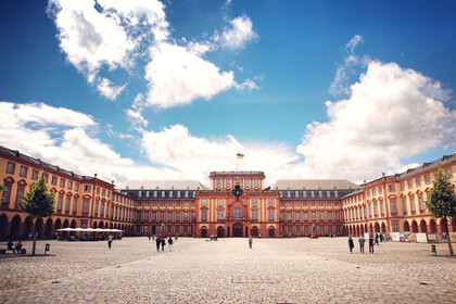 Das Barock-Schloss und der Ehrenhof der Universität Mannheim unter strahlend blauem Himmel. Das Schloss ist von unzähligen Fenstern, rotem Sandstein und einer gelben Fassade geprägt.