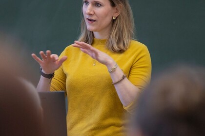 Clara Solzbacher steht vor einer grünen Tafel und gestikuliert mit den Händen.