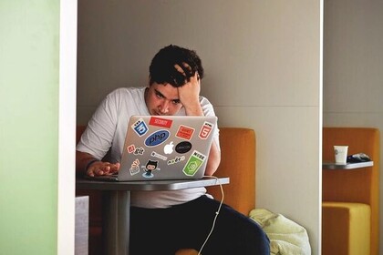 Ein Student mit dunklen Haaren und einem weißen T-Shirt, sitzt vor seinem Laptop. Unten rechts ist das Logo des IFS- Institut für Sport der Universität Mannheim.