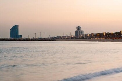 Strandpanorama bei Sonnenuntergang mit ruhigem Meer, Barcelonas Skyline und dem markanten W-Hotel im Hintergrund.