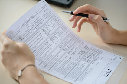Eine Person füllt einen Fragebogen aus, der auf einem Tisch liegt. In der rechten Hand hält sie einen Stift.