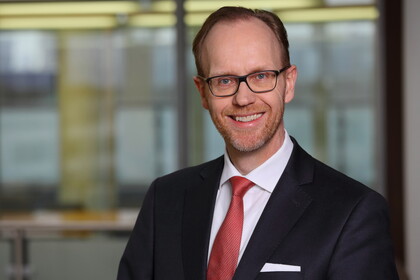 Prof. Dr. Lobin im Porträt mit schwarzem Anzug, weißem Hemd, roter Krawatte und schwarzer rechteckiger Brille in einem Büro