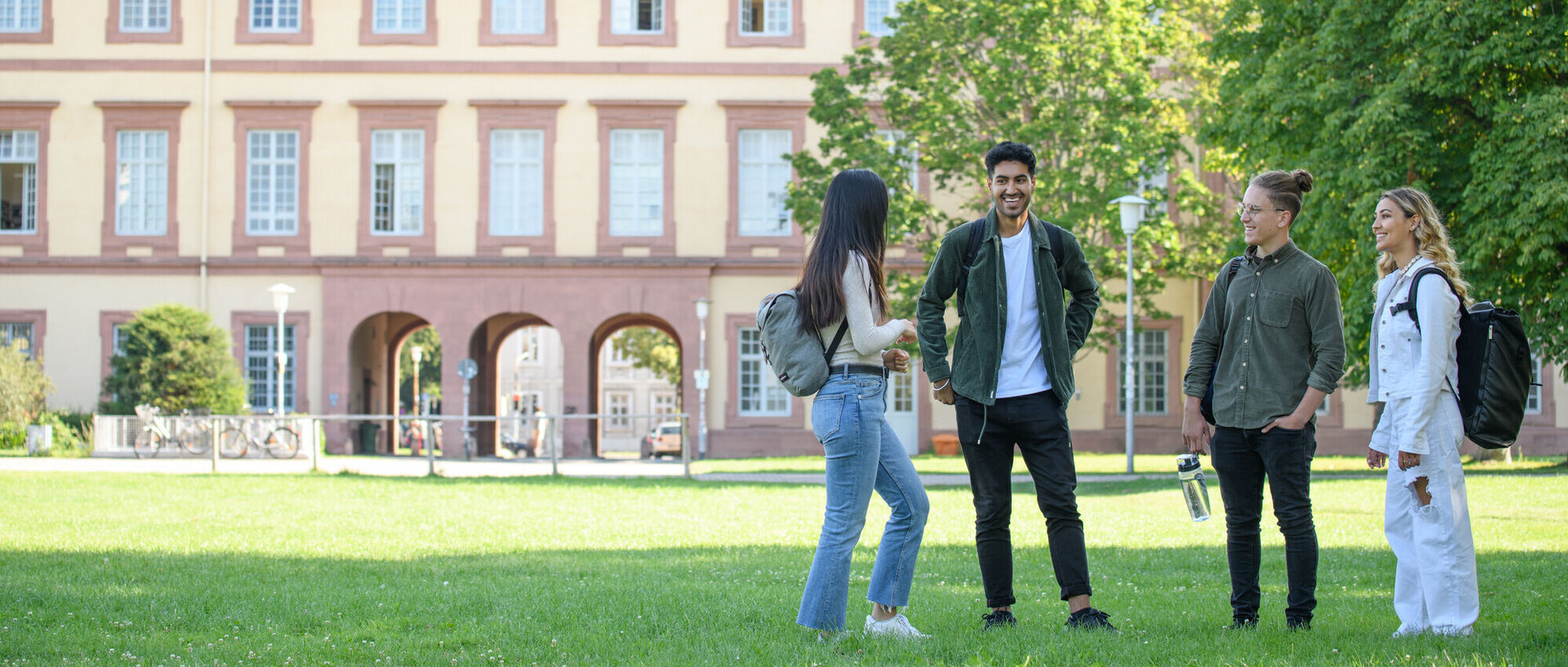 Studierende stehen vor dem Schloss auf einer Wiese