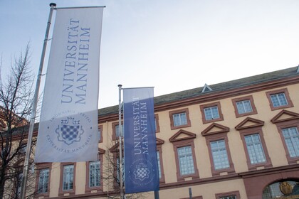 Blick auf die Universität Mannheim. Davor hängen zwei Fahnen mit dem Logo der Universität Mannheim