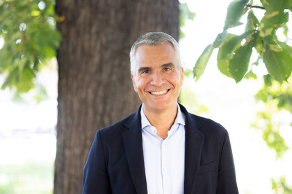 Prof. Dr. Thomas Fetzer. Breit lächelnd steht er vor einem Baum, dabei trägt er ein dunkles Jackett.