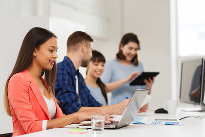 Vier Studierende sitzen an einem Tisch und unterhalten sich. Auf Dem Tisch steht ein Laptop.