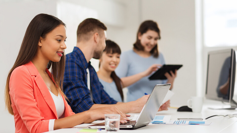 Vier Studierende sitzen an einem Tisch und unterhalten sich. Auf Dem Tisch steht ein Laptop.