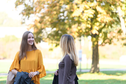 Zwei Studierende lächeln. Im Hintergrund ist ein großer Baum. 