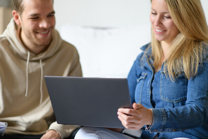 Eine junge Frau zeigt einem jungen Mann etwas auf dem Laptop.