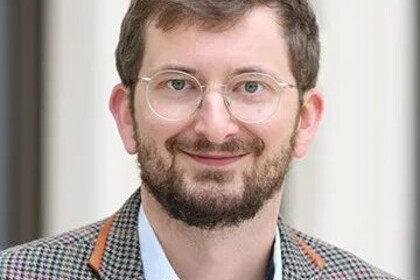 Portrait von Philipp Müller. Er trägt eine Brille, ein weißes Hemd und ein braunes, kariertes Sakko.