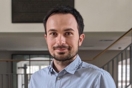 Renat Shigapov in einem Korridor. Er hat kurze dunkle Haare, einen Bart und trägt ein grau-gestreiftes Hemd.