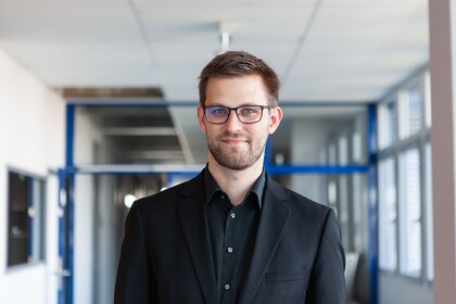  Dr. Stefan Janke hat kurze braune Haare, einen Bart und eine Brille. Er trägt ein schwarzes Jacket und ein schwarzes Hemd.