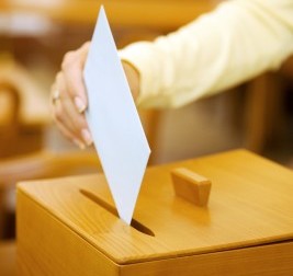 Eine Frau steckt einen weißen Briefumschlag in eine Wahlurne.