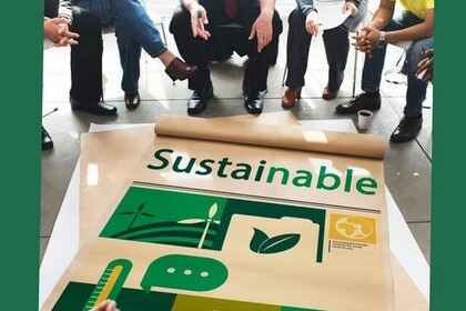 Auf dem Boden liegt ein Plakat mit der Aufschrift "Sustainable". Viele Personen sitzen davor. Oben links steht "Green Uni Ma"